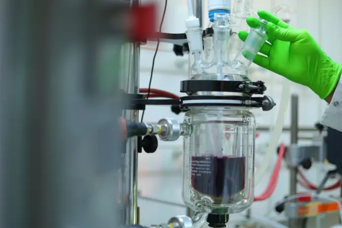 Scientist adjusting a jacketed glass reactor containing a purple solution.